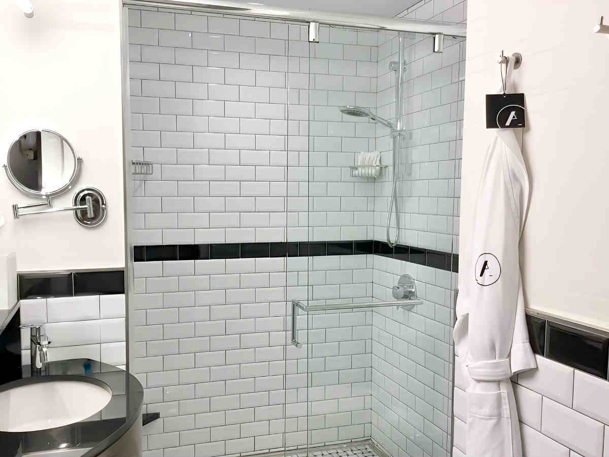 Beautiful Walk-In Shower with White Tile and a Robe at the Archer Hotel in NYC